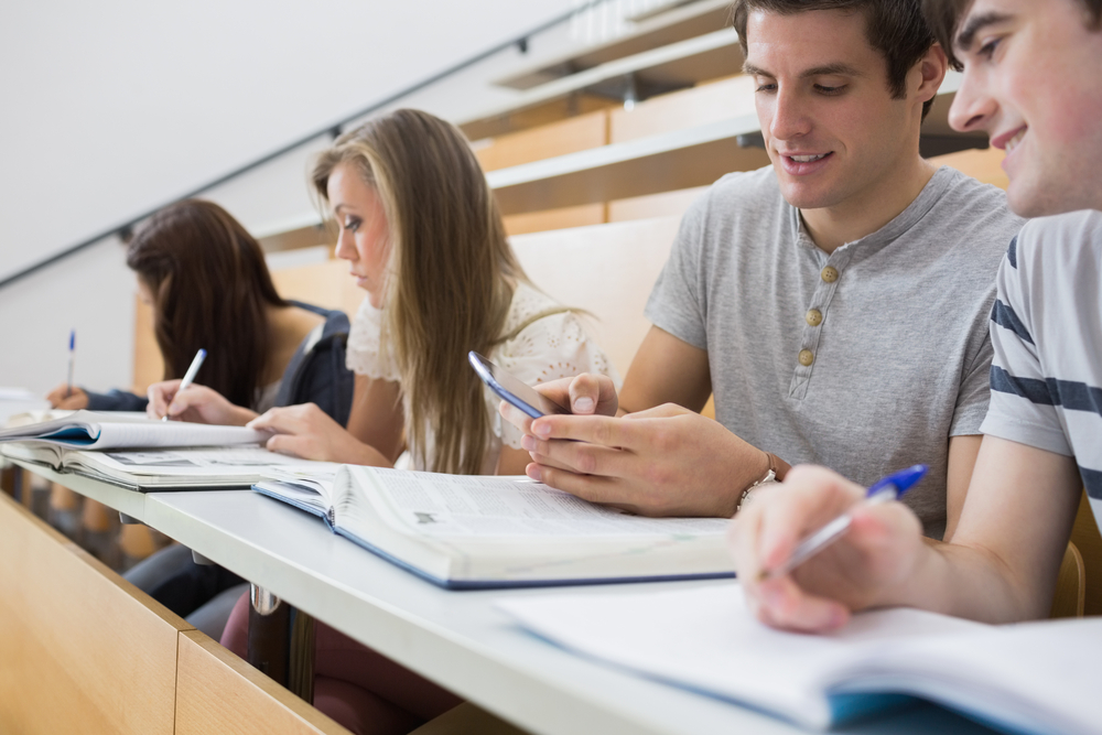 Student smiling and showing friend smartphone in lecture hall